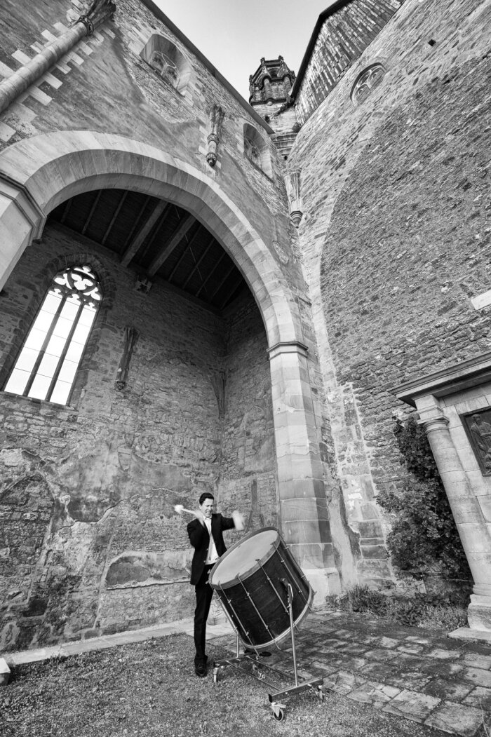 Ausstellung „Barfüßerkirche Erfurt – Von Feiniger zum Totentanz“ Schwarz Weiß Aufnahme eines alten Gebäudes, im Vordergrund ein Mann im Anzug und eine Trommel