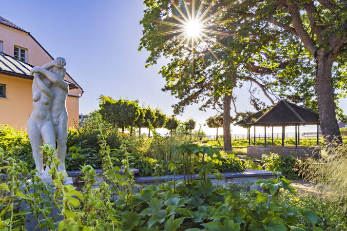 Blick in einen Garten mit Sonne und einer Skulptur