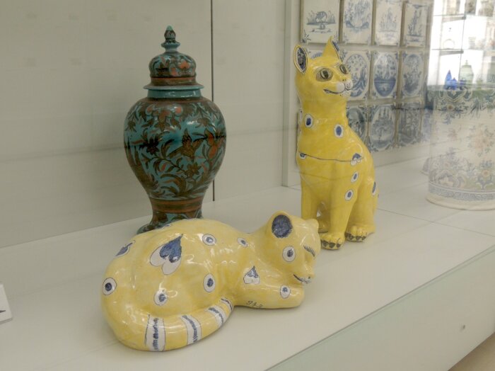 Zwei Katzen von Émile und Charles Gallé, um 1864, Fayencesammlung Glasvitrine mit zwei gelben Figuren in Katzenform un dahinter einer Vase