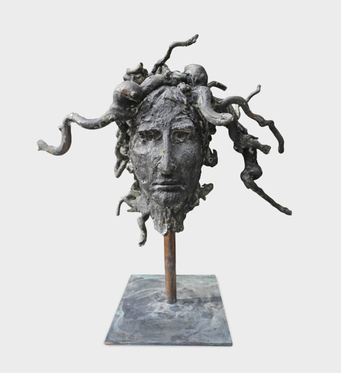 Medusa, 2023, 37 x 37 x 25 cm, Bronze Eine graue Skulptur mit einem Kopf aus dem schlangenartige Haare kommen auf einem eckigen Sockel