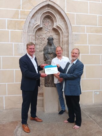 drei Männer halten einen symbolischen Scheck in der Hand