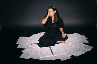 Foto: Sängerin und Komponistin Diana Syrse © Astrid Ackermann Portrait einer sitzenden Frau auf Blättern mit Noten