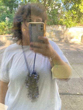Eine Frau fotografiert sich selbst im Spiegel und trägt eine Kette.