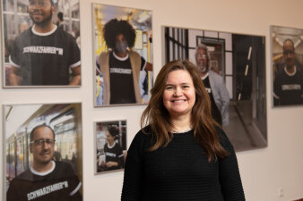 Lächelnde Frau steht vor einer Wand mit mehreren aufgehangenen Fotografien