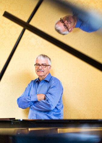 Foto: Der Schweizer Komponist Max E. Keller © Stefan Kubli Portrait eines älteren Mannes im blauen Hemd vor gelber Wand