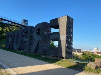 Schriftzug von hinten im Hintergrund eine Stadt und Bäume