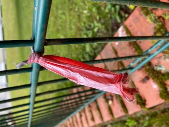 Rote Plastiktüte hängt an einem grünen Zaun