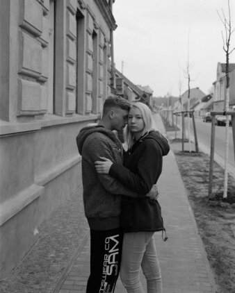 Foto: Ute Mahler, Werner Mahler, aus der Serie Kleinstadt, 2015–2018, Silbergelatine-Abzug © Ute Mahler, Werner Mahler Eine junge Frau und ein junger Mann stehen sich umarmend in einem Straßenzug