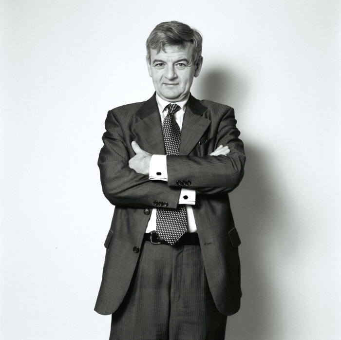 Portrait von Joschka Fischer (1998) Schwarz-Weiß-Foto eines älteren Mannes in einem dunklen Anzug vor einer weißen Wand