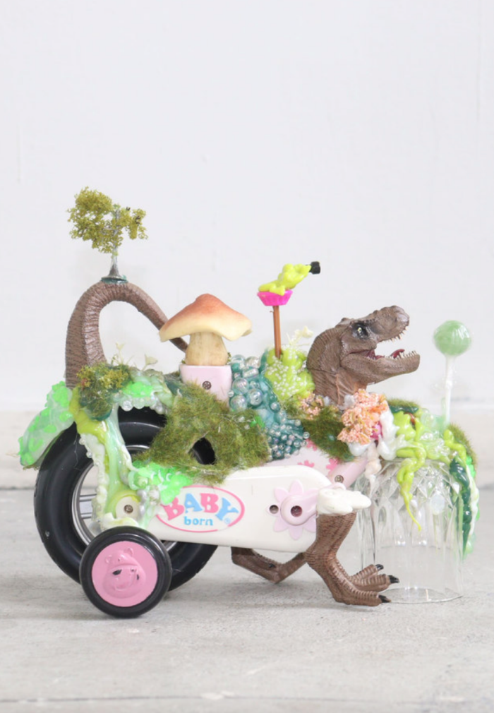 Lisa Mayer aka Hypernormalisa, Rolldino, 2024, Plastik, Spielzeug, Kunstmoos, Heißkleber, ca. 25 × 15 × 10 cm Buntes Objekt aus verschiedenen Elementen wie Rollen, Gräsern, einem Dino, einem Lolli und weiteren