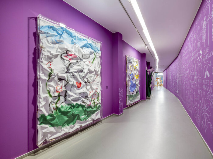 Blick in die Ausstellung „The Cute Escape. Empathie, Empowerment, Empfindsamkeit“ Blick in einen lila Gang mit Schrift und Gemälden