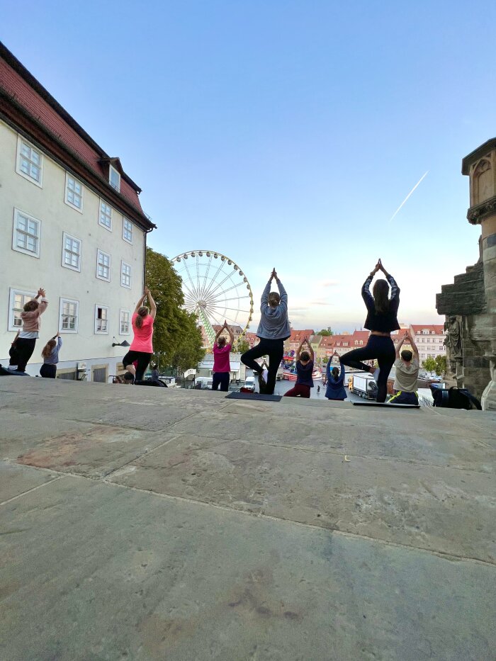 Altstadtyoga auf dem Domstufen Menschen stehen auf einer Treppe in Yoga-Pose, im Hintergrund Häuser und ein Riesenrad