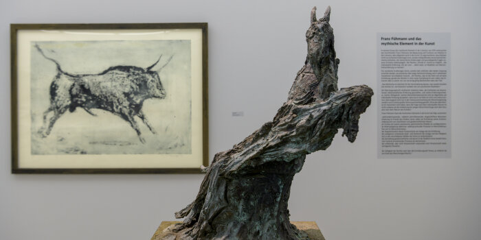 eine Skulptur, im Hintergrund eine Wand mit Zeichnung eines Stiers und Ausstellungstext