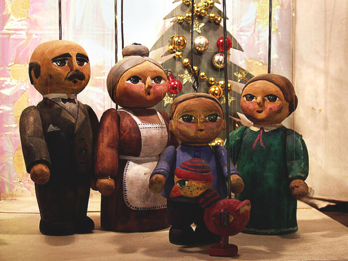 Szene aus dem Puppenspiel „Die Weihnachtsgans Auguste“ Verschiedene Puppen aus Holz mit einem Weihnachtsbaum aus Holz im Hintergrund