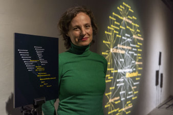 Foto: Antje Seeger in ihrer Ausstellung „Knoten gegenüber Kanten. Wunderkammer mit Videos, digitalen Grafiken und Fotografien“ © Stadtverwaltung Erfurt Eine Frau zwischen zwei Installationen