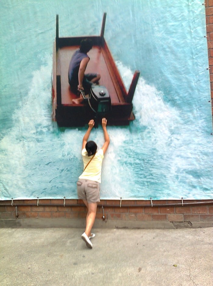 Foto einer Frau, die an ein Plakat fasst, auf dem ein umgedrehter Tisch als Motorboot auf dem Meer schwimmt