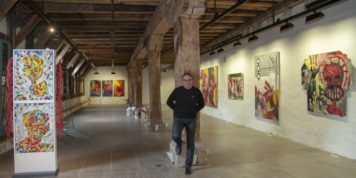 Ein Mann lehnt an einem Holzbalken, an den Wänden hängen gemalte Bilder
