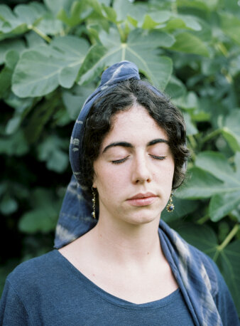 Junge Frau mit Haarband und geschlossenen Augen vor grünen Blättern
