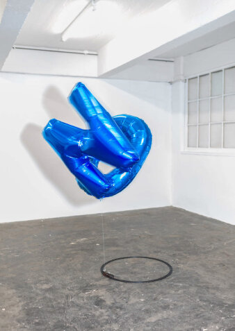 Foto: Franziska Paula Wolber, N O (Loop 8 Sekunden), 2018, batteriebetriebene Eisenbahn, Heliumballons, 195×68×68 cm © Jakob Adolphi Zwei blaue Luftballons an einer Modelleisenbahn in einem hellen Raum