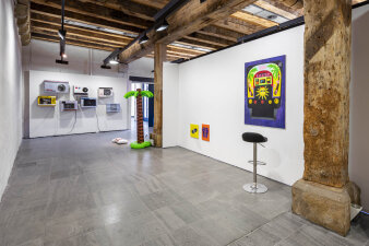 Blick in einen Raum mit bunten Ausstellungsgegenständen an der Wand und auf dem Boden