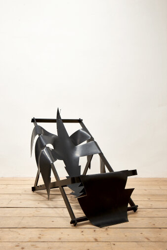 Blick auf einen Liegestuhl mit schwarzem Stoff in Form einer Palme darauf. Darunter Holzfußboden