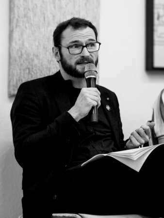 Foto: Schriftsteller Mario Osterland © Andrea Vollmer Schwarz-Weiß-Aufnahme eines Mannes mittleren Alters, der in ein Mikrofon spricht