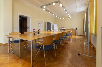 hell erleuchteter Raum mit Tischen in Form einer großen Tafel in der Mitte