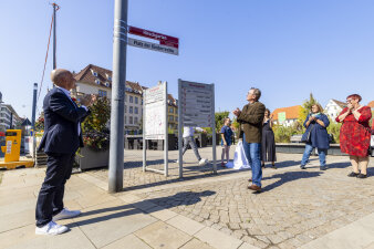 mehrere Personen klatschen und betrachten ein rot-weißes Straßenschild