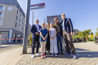 mehrere Personen, darunter zwei Kinder, stehen vor einem rot-weißen Straßenschild