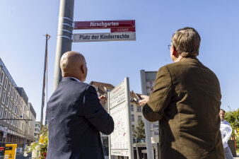 zwei Männer applaudieren und betrachten ein rot-weißes Straßenschild