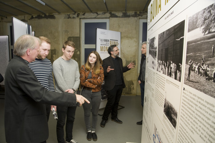 Führung durch die Ausstellung „Die I.G. Farben und das KZ Buna-Monowitz“ Ein Mann erklärt jungen Menschen etwas in einer Ausstellung.
