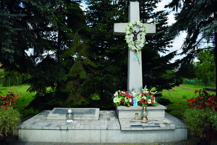 Denkmal für die in Buna-Monowitz ermordeten KZ-Häftlinge Ein Kreuz und eine Gedenktafel mit Blumen geschmückt.