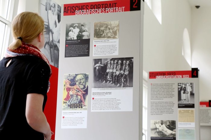 Blick in die Ausstellung "Marlene Dietrich. Die Diva. Ihre Haltung. Und die Nazis." Eine Frau betrachtet eine Ausstellungstafel. Im Hintergrund sind weitere Ausstellungstafeln zu erkennen.