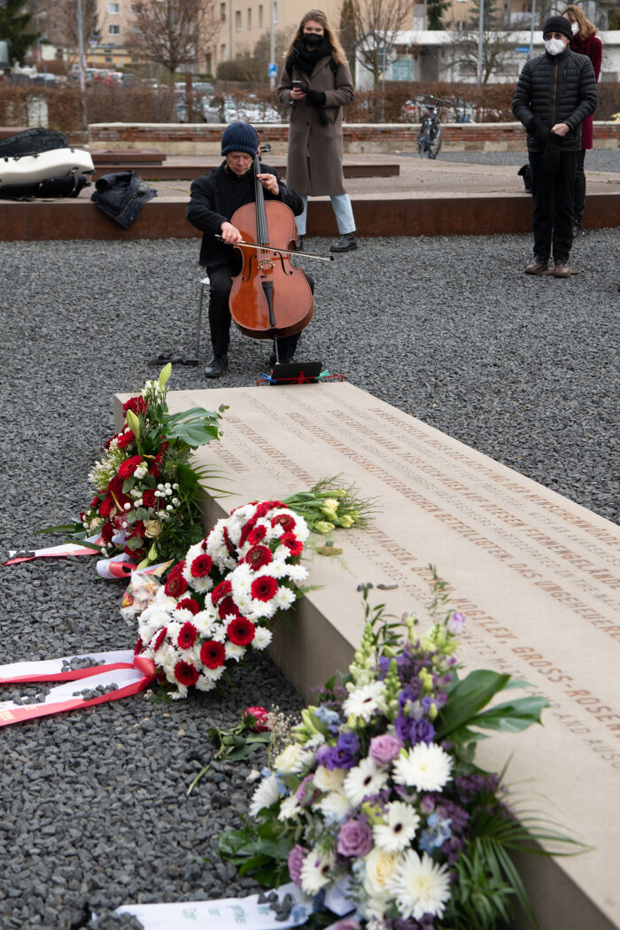 Gedenken am Stein der Erinnerung Person mit Cello, an einem Gedenkstein mit Blumen