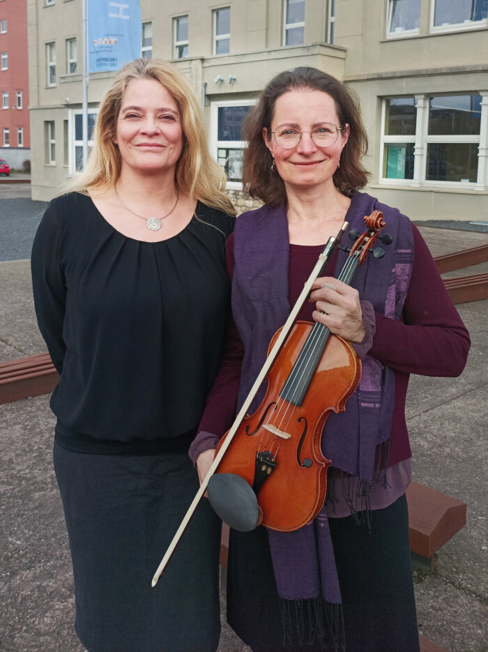 zwei Frauen stehen nebeneinander, eine hält eine Violine