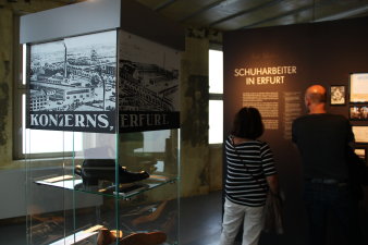 Im Vordergrund steht eine Ausstellungsvitrine, im Hintergrund betrachten Besucher Ausstellungstafeln. 