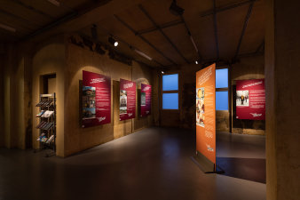 7 Ausstellungstafeln stehen im Raum, an den Wänden hängen weitere Tafeln. Eine Nische mit Flyerständer.