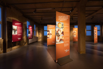 Mehrere Ausstellungstafeln stehen im Raum, an den Wänden hängen weitere Tafeln. 