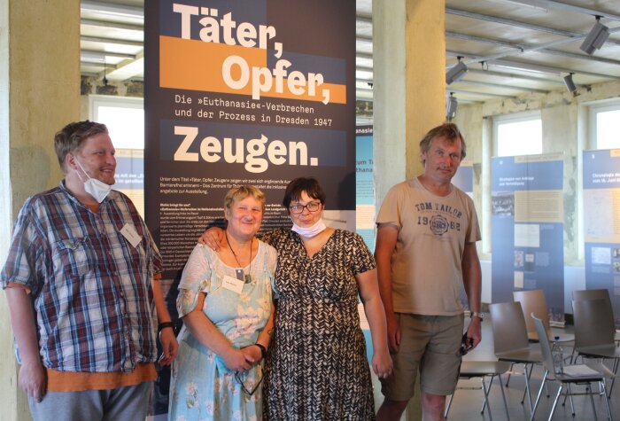 Tandemführung in Leichter Sprache in der Sonderausstellung 2022 Vier Personen stehen vor einem Banner der Sonderausstellung "Täter, Oper, Zeugen"