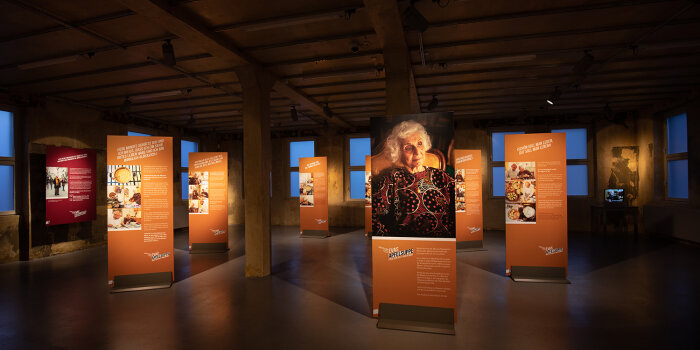 Foto: Blick in die Ausstellung "Évas Apfelsuppe oder der Duft von Heimat" © Norman Hera 7 Ausstellungstafeln stehen im Raum, an den Wänden hängen weitere Tafeln.