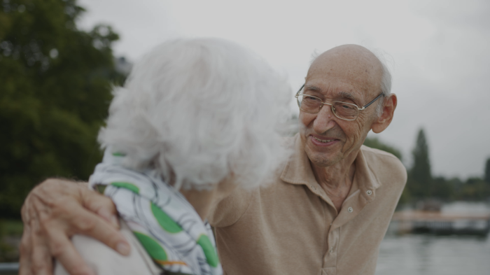 Farbfoto. Älterer Mann umarmt ältere Frau.