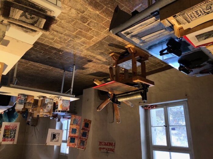Einsicht in die Druckwerkstatt Gefließter Raum mit Druckmaschinen, Walzen, Papier und individuellen Kunstdrucken an einer Leihne aufgehängt