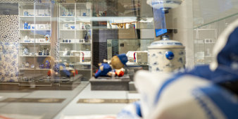 Foto: Blick in die Sonderausstellung „Blau und Blaues“ im Volkskundemuseum © Stadtverwaltung Erfurt Blick durch eine Vitrine, in der eine blaue Puppe liegt, auf einen Schrank mit blauem Geschirr