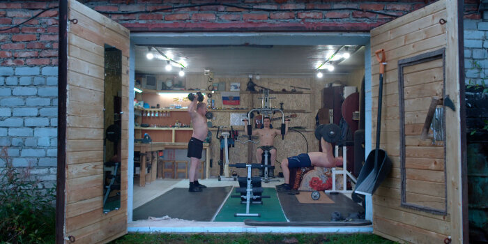 drei Männer trainieren an Fitnessgeräten in einer Garage